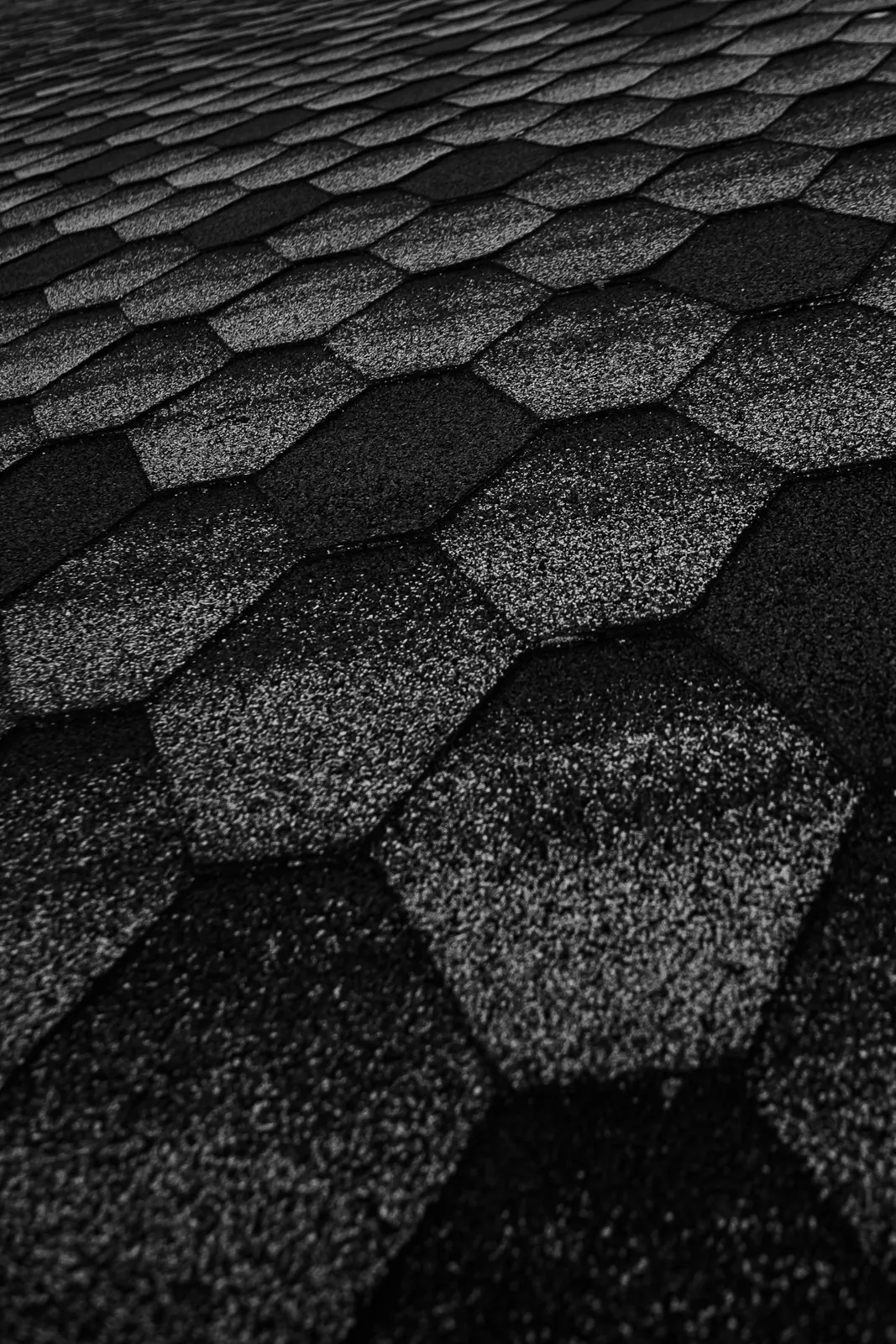 Hexagonal asphalt shingles in dark tones covering a roof slope