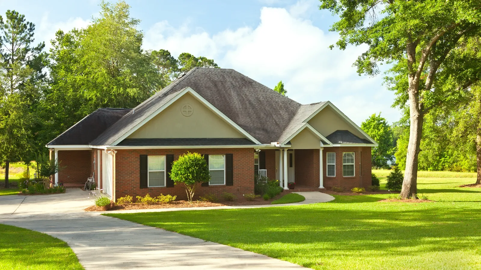 Gray shingle roof on a brick ranch home shaded by mature trees